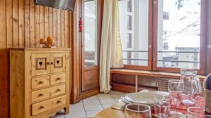 A wooden interior with a TV, wooden cabinets, a dining table set with glasses, and a window with a view of buildings.