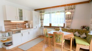 A compact kitchen with white cabinets, a wooden countertop, and a dining area with a table and chairs. - Christl by Interhome (Fügen)