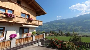 A wooden chalet with a balcony, large windows, and a view of green hills and mountains. - Christl by Interhome (Fügen)