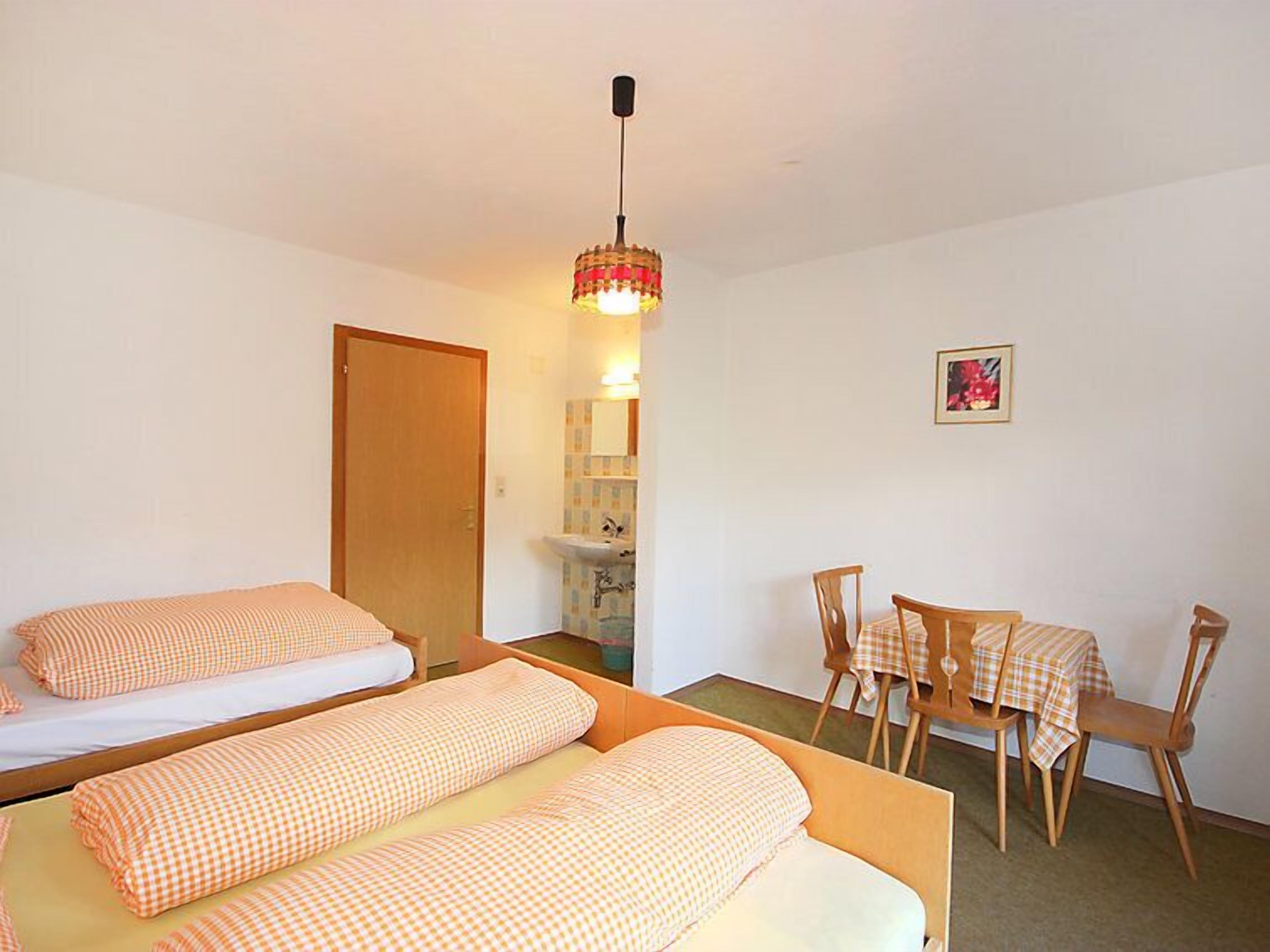 A room with two beds, a wooden table with a checkered tablecloth, and a hanging light fixture.