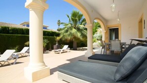A covered outdoor seating area with a sofa and lounge chairs, surrounded by palm trees and a hedge. - Casa Kate by Interhome (Calpe/Calp)