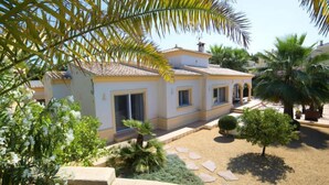 A two-story house with a tiled roof, a covered patio, and a garden with palm trees and shrubs. - Casa Kate by Interhome (Calpe/Calp)