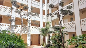 Un immeuble à plusieurs étages doté d’une cour intérieure, entourée de diverses plantes et d’arbres.