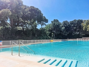 A swimming pool with clear blue water, surrounded by a white fence and trees.