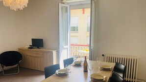 Uma área de refeições com mesa de madeira posta para dois, um laptop num escritório e vista para a varanda.