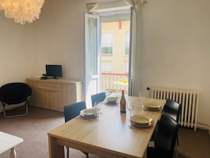 Ein Essbereich mit einem Holztisch, gedeckt für zwei Personen, einem Laptop auf einem Schreibtisch und Blick auf den Balkon.