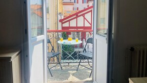 Varanda com mesa e cadeiras, guarda-corpo vermelho e vista para edifícios vizinhos.
