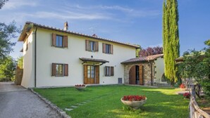 A two-story house with a stone extension, a well-maintained lawn, and a tall tree. - Apartment Lucia by Interhome (Bucine)