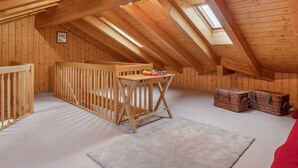 Een zolderkamer met hoge plafonds, houten balken, een wieg, een tafel met speelgoed en rieten manden.