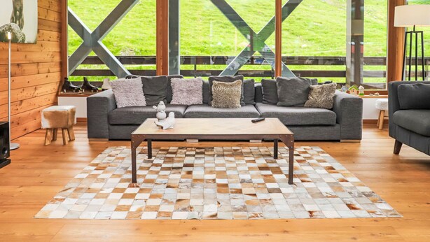 Uma sala de estar moderna com uma janela grande, piso de madeira e tapete xadrez.