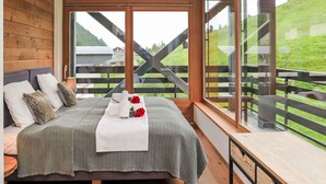 Quarto com cama grande, paredes de madeira e varanda com vista para uma paisagem verde.