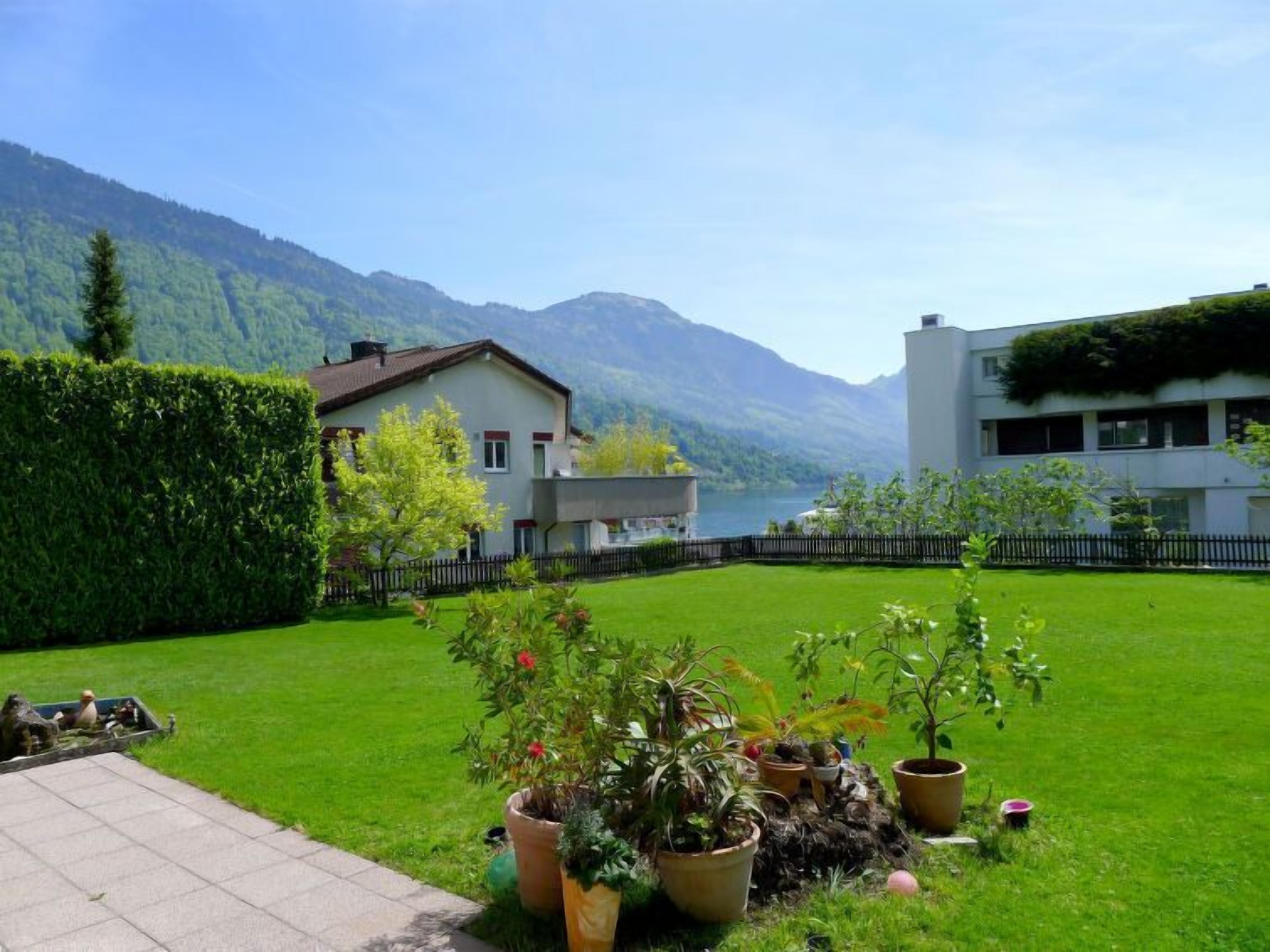 A serene residential area with a well-maintained lawn, potted plants, and a view of a lake and mountains.