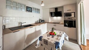 Una cucina moderna con mobili bianchi, un piano di lavoro in legno, un lavello, un forno a microonde e una televisione sopra il forno.