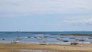 Una spiaggia con diverse imbarcazioni ancorate in acque basse, un litorale sabbioso e una costa lontana con un molo di protezione.