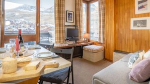Une pièce chaleureuse avec un plafond en bois, une table à manger dressée avec des assiettes et des verres, un téléviseur et une vue sur un paysage montagneux.