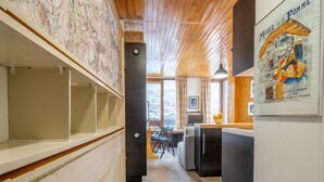 Un couloir étroit aux murs en bois et au plafond bas, qui mène à une salle à manger offrant une vue sur l’extérieur.