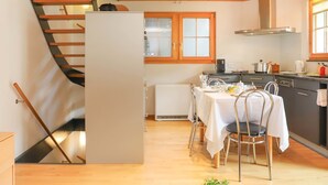 Una cocina moderna con armarios de madera, una mesa de comedor con sillas y una escalera con barandilla de madera.