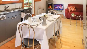 Un comedor con una mesa preparada para cuatro, una cocina con electrodomésticos modernos, una chimenea y una sala de estar acogedora con un sofá rojo.