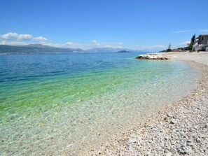 A pebble beach with clear water and a building on the right.