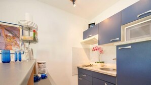 Una cucina moderna con mobili blu scuro, un piano di lavoro bianco, un forno a microonde e un lavello. Sopra il lavello c'è una piccola mensola e un quadro appeso al muro.