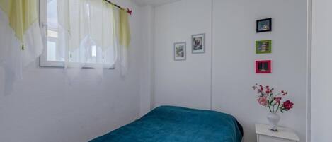 Un dormitori amb un llit individual, una tauleta de nit, una finestra amb cortines i una paret amb quadres emmarcats.