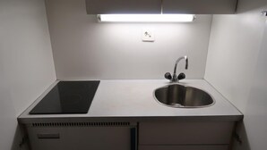 Una cuineta compacta amb fogó integrat, un rentapeus d'acer inoxidable i un petit armari amb calaixos.