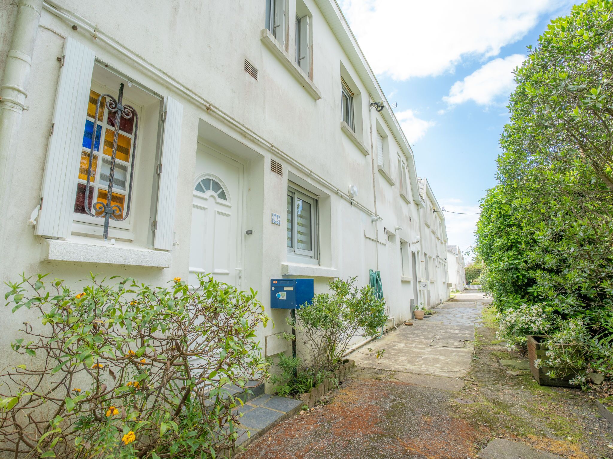 A row of white buildings with a narrow alleyway between them, surrounded by greenery and a clear sky.