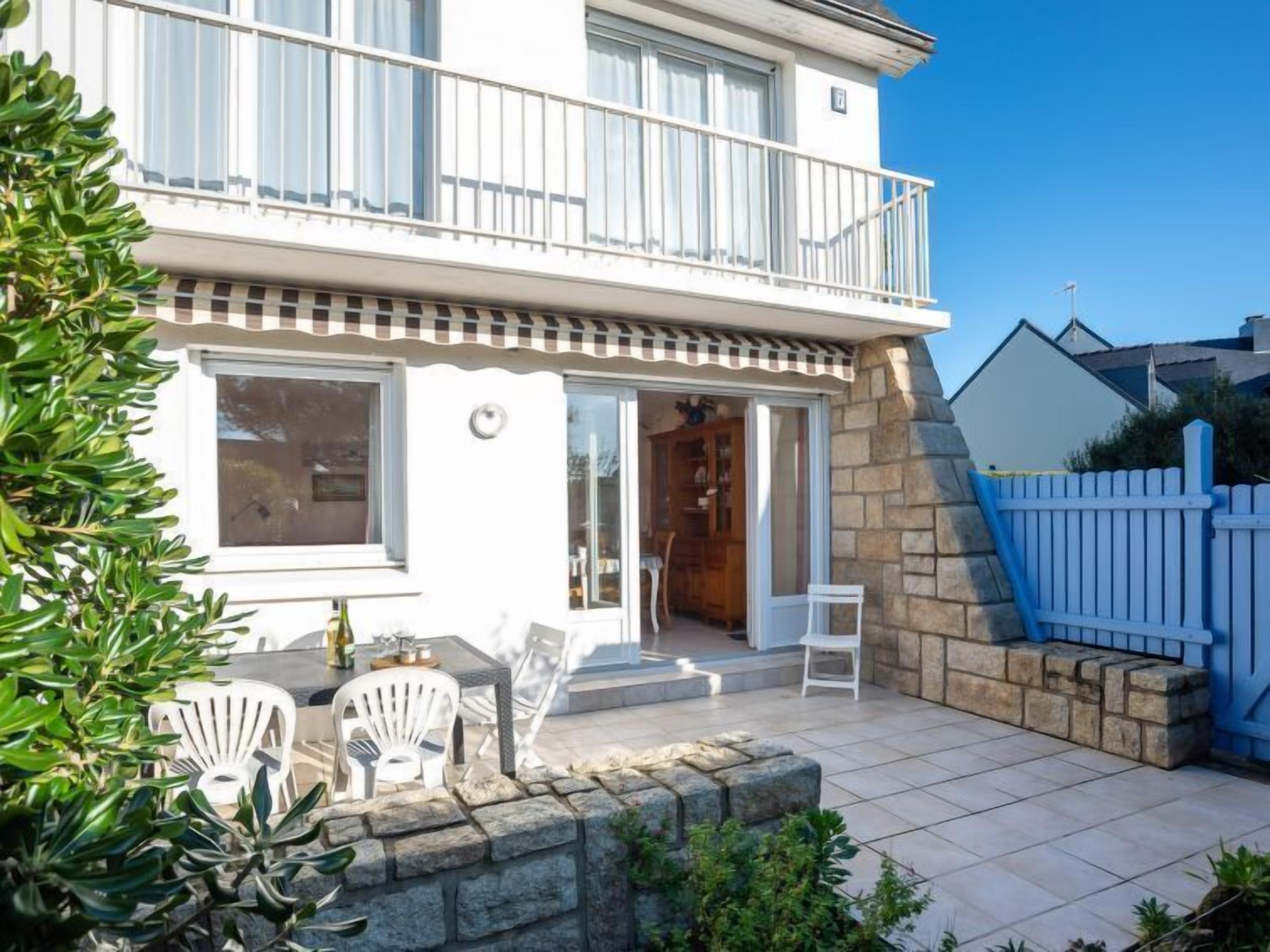 Ein zweistöckiges Haus mit einem Balkon, einer Terrasse mit Stühlen und einer Steinmauer.