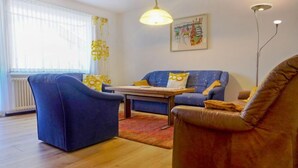 Ein Wohnzimmer mit blauem Sofa, braunem Sessel, Couchtisch aus Holz und einer Stehlampe.
