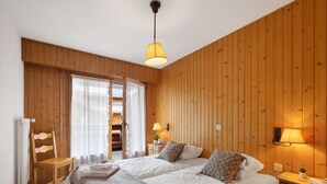 Une chambre confortable avec deux lits, des murs en bois, un luminaire au plafond et une fenêtre avec des rideaux.