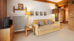 Un salon chaleureux avec un canapé beige, des meubles en bois, un radiateur et des tableaux accrochés au mur.