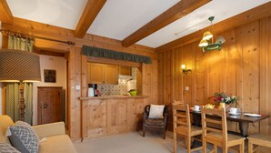 L’intérieur d’un chalet en bois chaleureux et accueillant, avec un coin repas, une cuisine et un canapé agrémenté de coussins à motifs.
