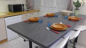 Una cocina con encimera gris, armarios blancos, microondas y un comedor con mesa preparada para cuatro.