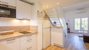 Een moderne keuken met witte kastjes, een ingebouwde oven en een koelkast. Er is een houten aanrecht en een mandje erop. Een trap leidt naar een balkon met uitzicht op groen.