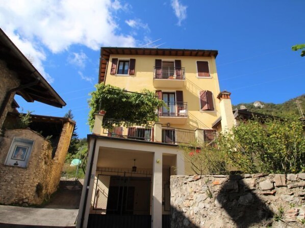 A multi-story building with a yellow facade, balconies, and a stone wall in the foreground. - Formaga by Interhome (Gargnano)
