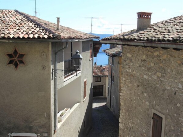 A narrow alleyway with traditional stone buildings, a star-shaped emblem on one building, and a clear view of the sky and mountains in the distance.