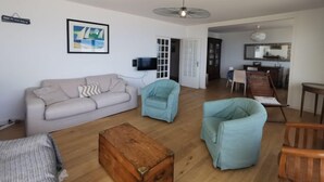 Een woonkamer met een bank, twee fauteuils, een houten salontafel, een televisie en een plafondventilator.