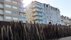 Een rij meerverdiepingsgebouwen met balkons, een houten hek op de voorgrond en een heldere lucht.