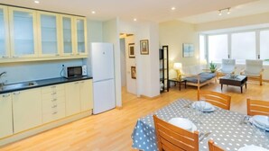 A compact apartment with a kitchenette, a dining area with a table set for two, and a living area with a sofa and a coffee table.
