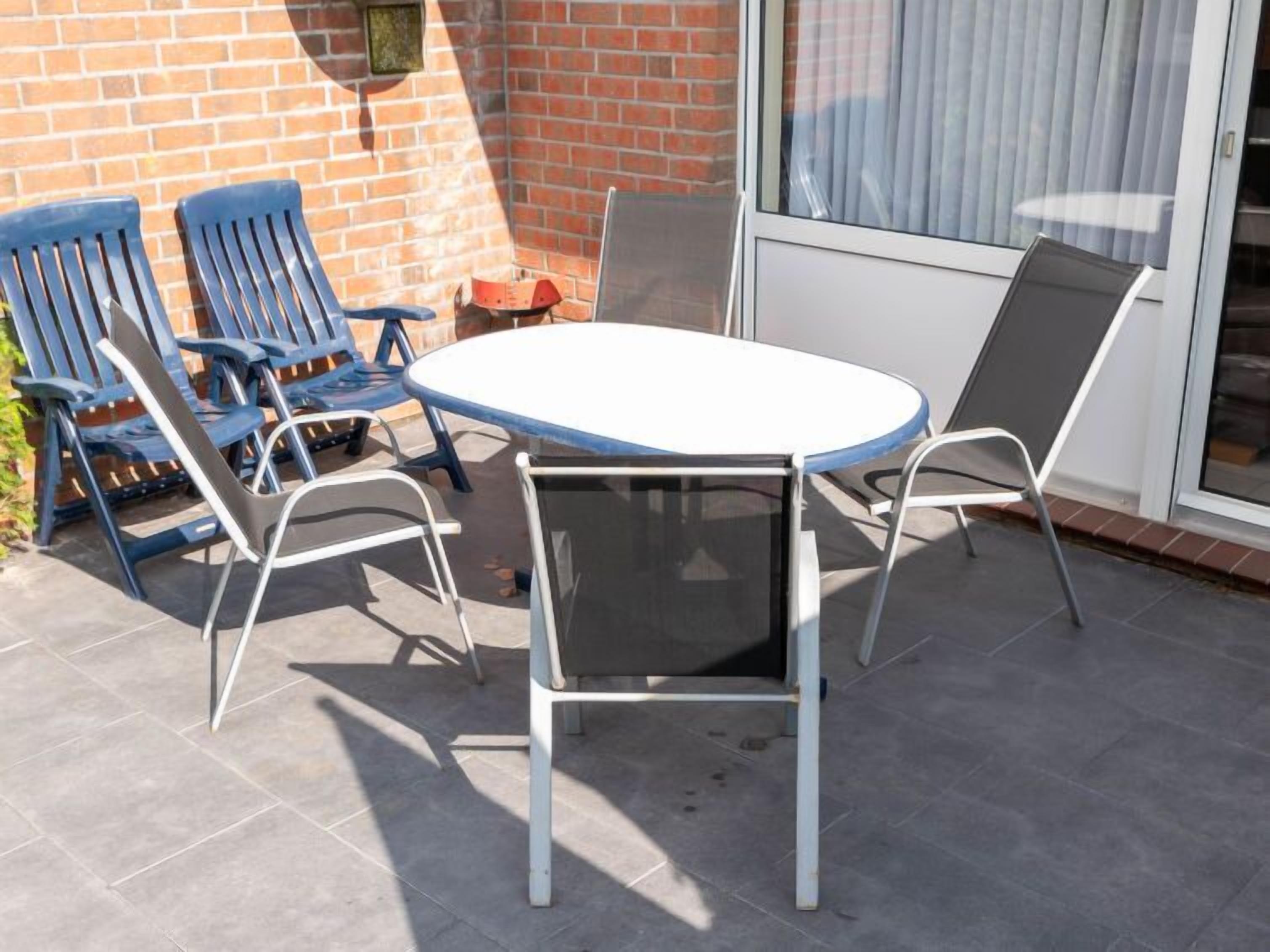 Een terras buiten met een ronde tafel en vier stoelen, een bakstenen muur en een schuifdeur met glas.