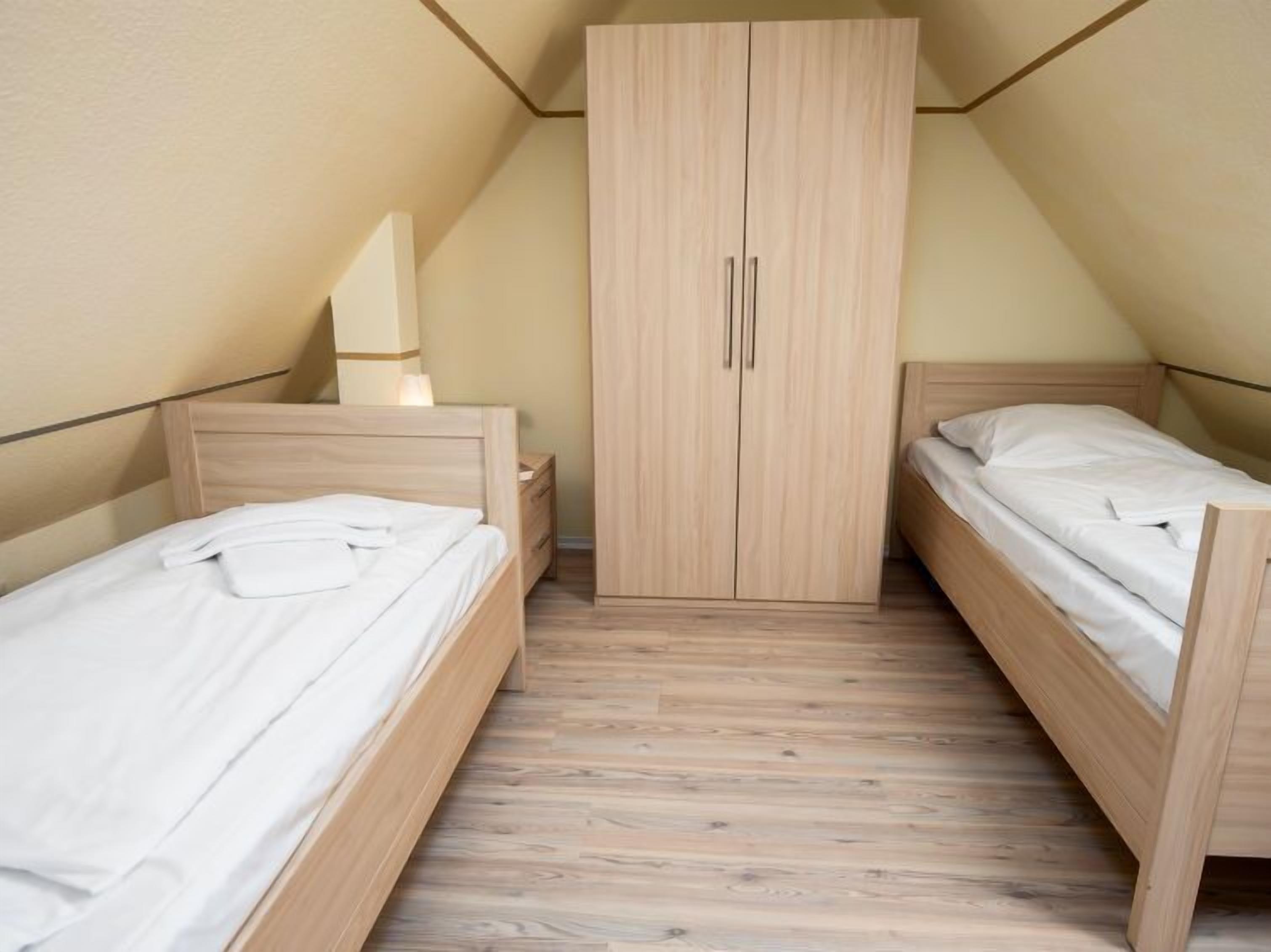 Een kleine, driekantige kamer met twee houten bedden, een garderobe en een nachtkastje.