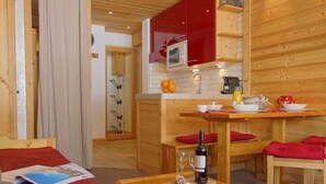 Une pièce chaleureuse avec un lit en bois, une petite table en bois sur laquelle se trouve une bouteille de vin, et un banc rouge.