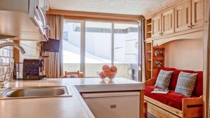 Une cuisine compacte comprenant un évier, un petit réfrigérateur et un coin repas avec une table et des chaises. Une fenêtre offre une vue sur l’extérieur.