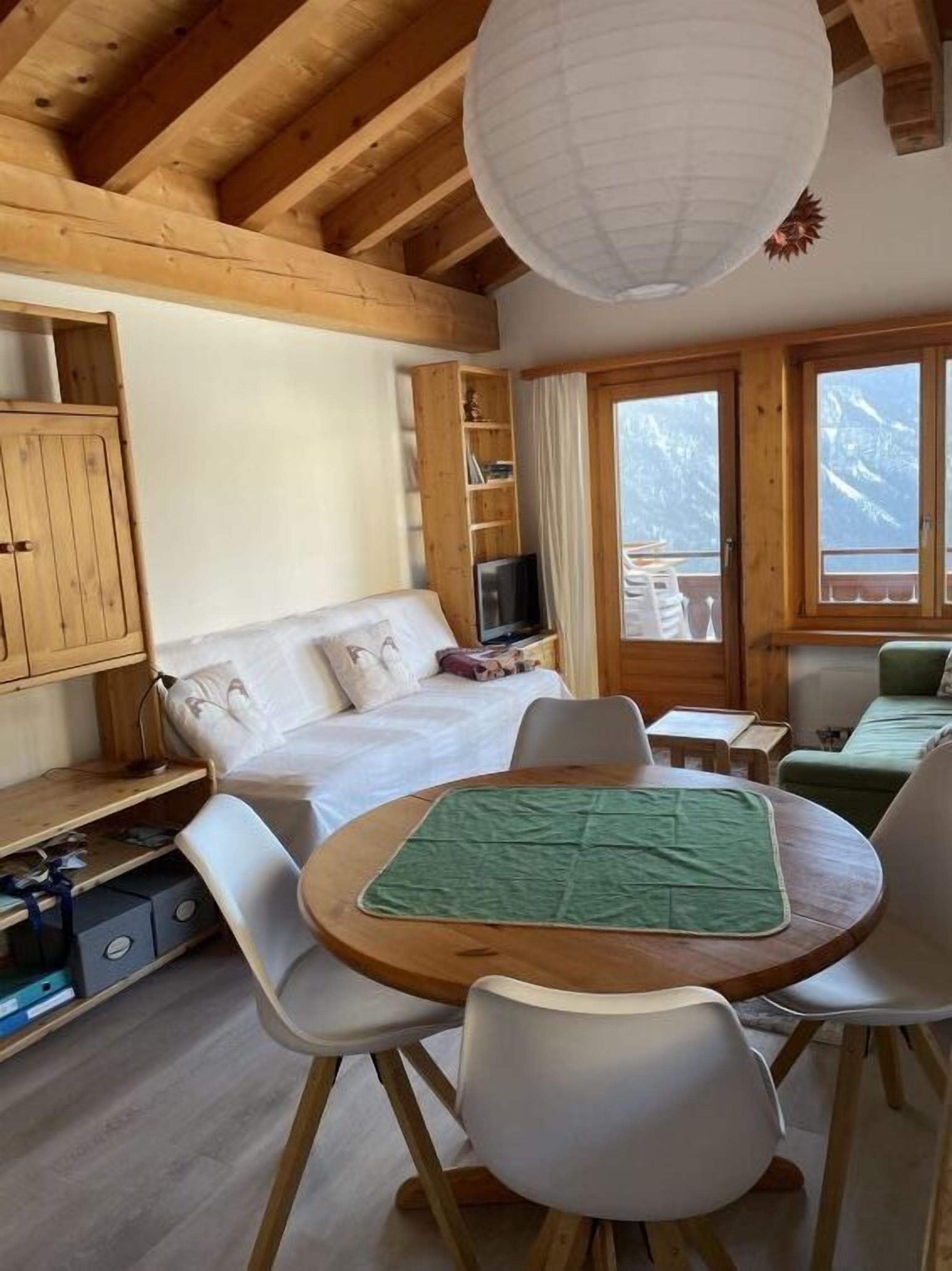 Una habitación acogedora con una cama, una mesa de comedor con sillas, un televisor y una ventana con vistas a montañas nevadas.