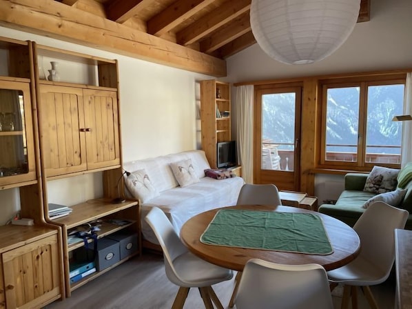 A cozy room with a bed, a TV, a dining table with chairs, and a view of the outdoors.