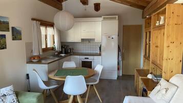 Une cuisine compacte avec des meubles blancs, un plafond en bois et un coin repas comprenant une table verte et des chaises blanches.