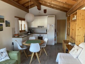 A compact kitchen with white cabinets, a wooden ceiling, and a dining area with a green table and white chairs.