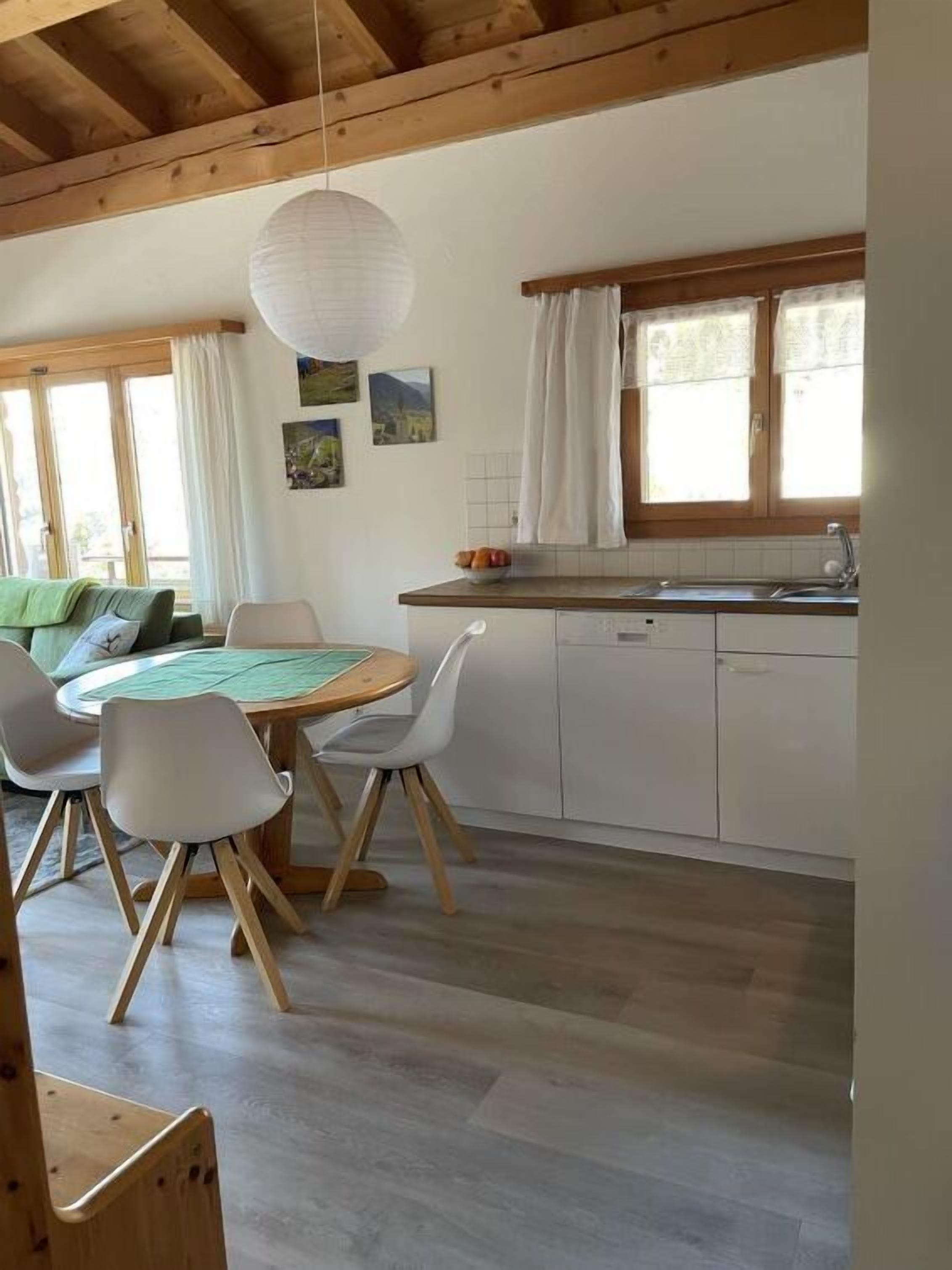 Une cuisine chaleureuse avec un coin repas, des poutres en bois, une table ronde et une vue sur l’extérieur.