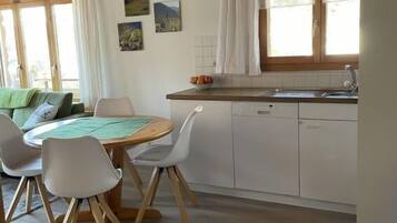 Une cuisine chaleureuse avec un coin repas, des poutres en bois, une table ronde et une vue sur l’extérieur.