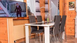 A wooden cabin with a dining area featuring a TV, a table, and chairs.